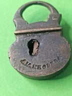 Miniature brass padlock held in fingers for scale