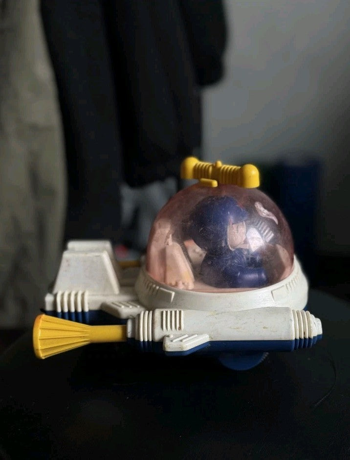 Cosmonaut toy figure in blue spacesuit inside pinkish dome cockpit